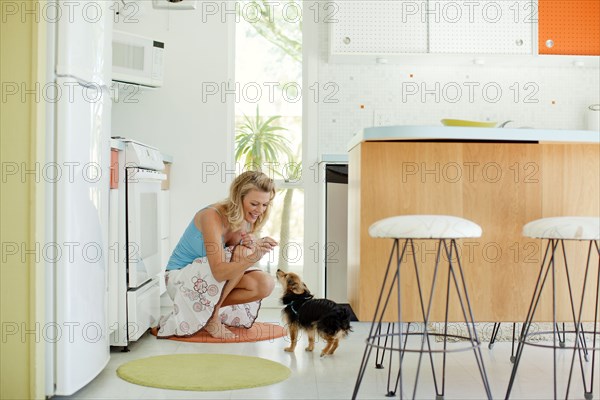 Caucasian woman feeding dog treat in kitchen