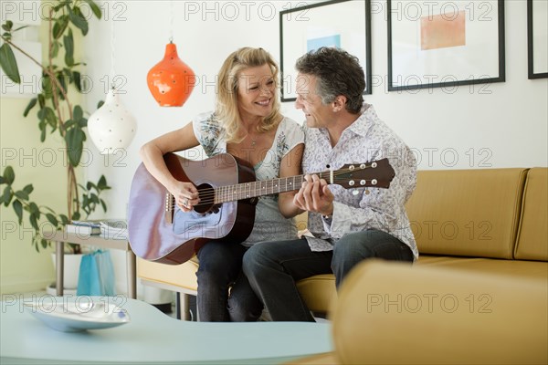 Man teaching wife to play guitar in living room