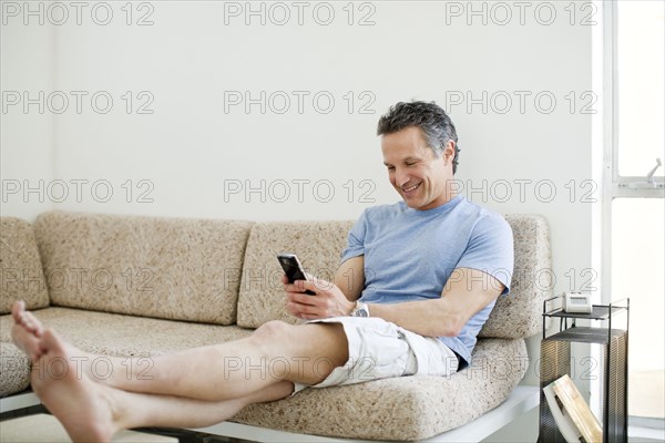 Smiling man text messaging on cell phone in living room