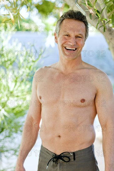 Smiling man in swim trunks standing outdoors
