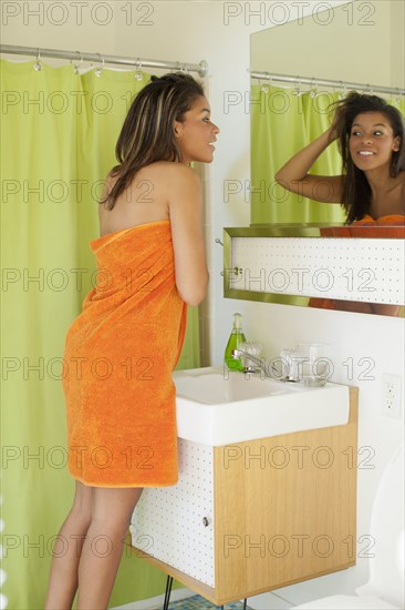 Mixed race woman wrapped in towel looking in mirror