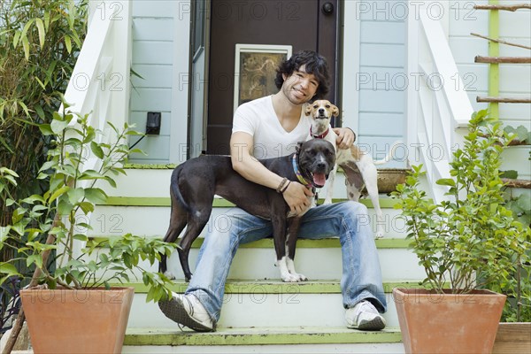 Mixed race man sitting on front stoop with dogs