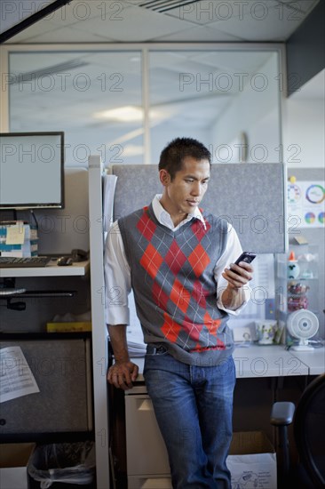 Mixed race businessman using cell phone in office cubicle