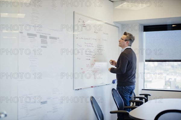 Caucasian businessman writing on whiteboard in conference room