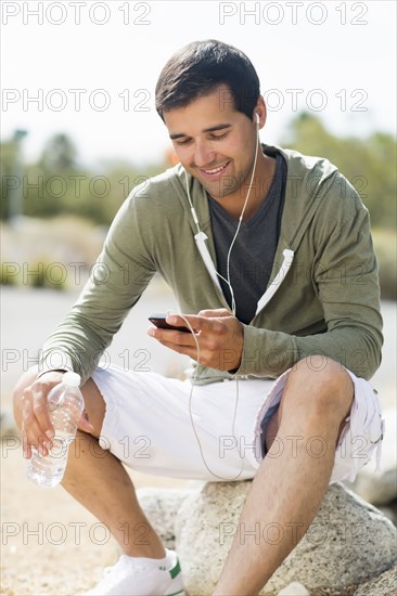 Mixed race man drinking water after exercise and listening to music