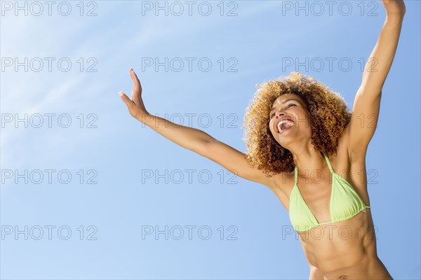 Mixed race woman in bikini with arms raised