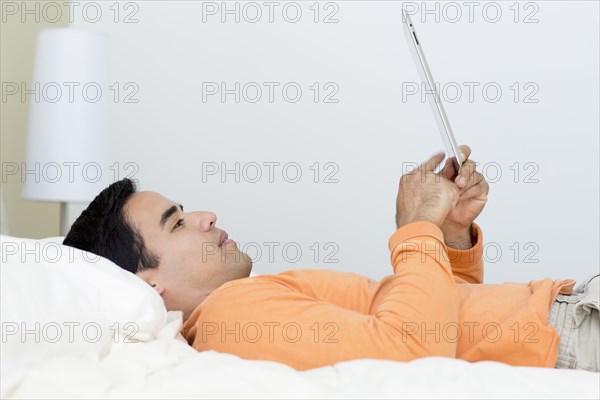Mixed race man laying in bed using digital tablet