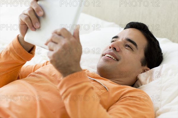 Mixed race man laying in bed using digital tablet