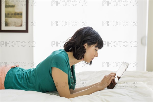 Mixed race woman laying on bed using digital tablet