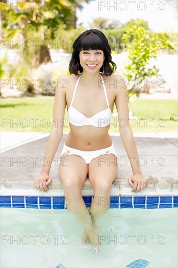 Mixed race woman with feet in swimming pool