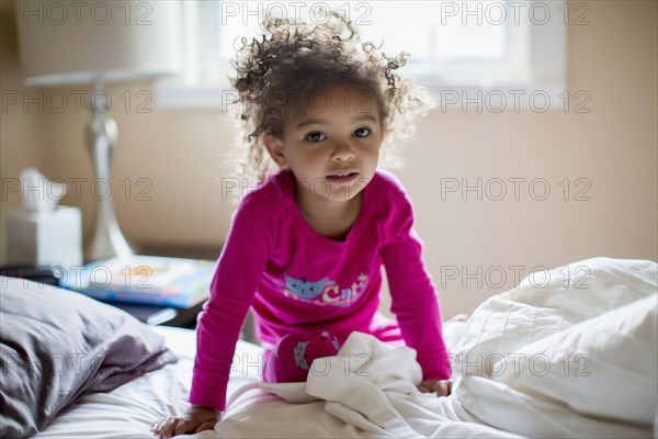 Mixed race girl kneeling on bed