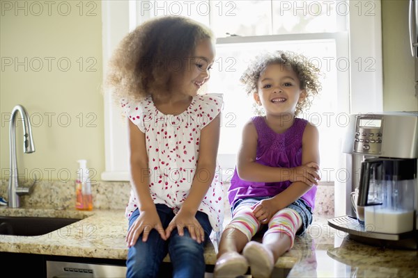 Mixed race sisters sitting on kitchen counter