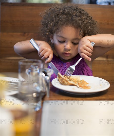 Mixed race girl eating breakfast in restaurant