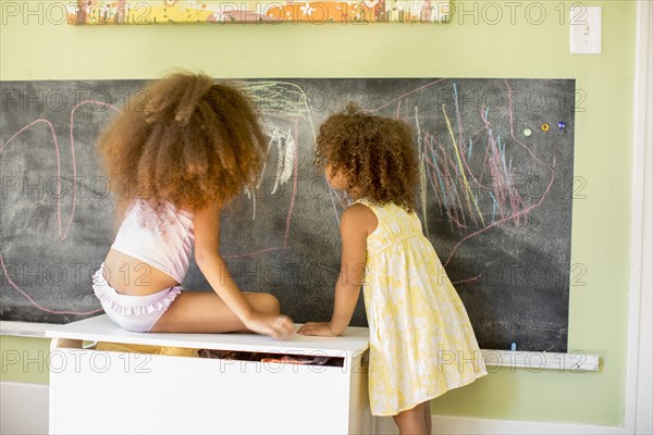 Mixed race girls writing on blackboard