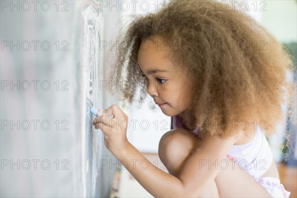 Mixed race girl writing on blackboard