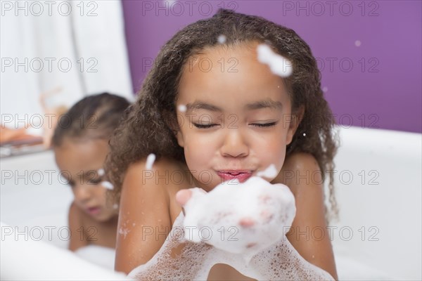 Mixed race girls playing with bubbles in bathtub