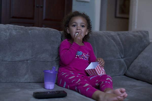 Mixed race girl eating popcorn and watching television