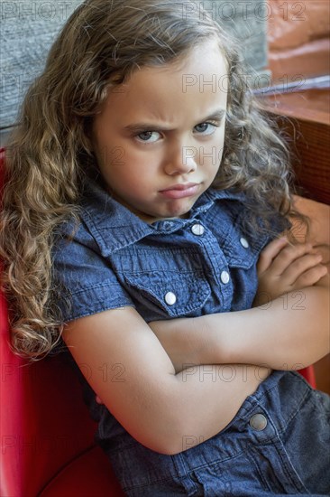 Frowning mixed race girl sitting in chair