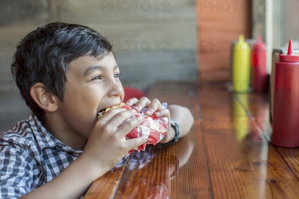 Mixed race boy eating burger in restaurant