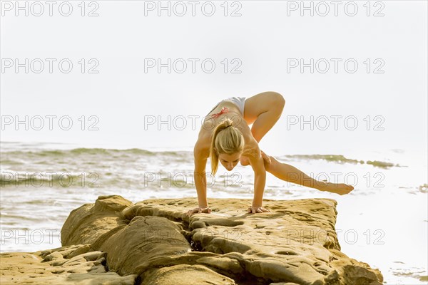 Caucasian woman practicing yoga on rocky beach