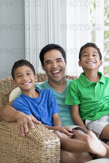 Hispanic father and sons sitting in armchair