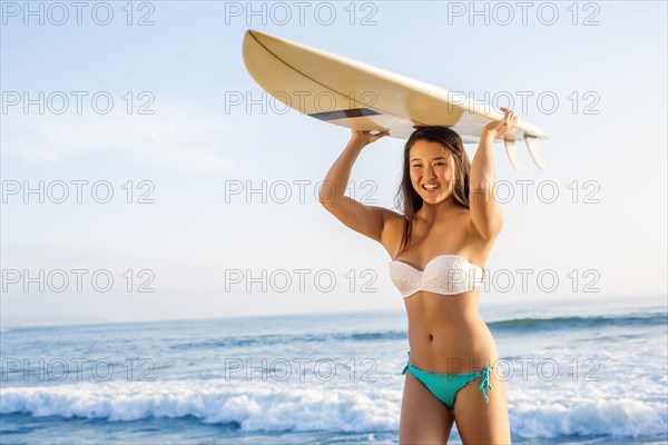 Japanese woman carrying surfboard overhead on beach