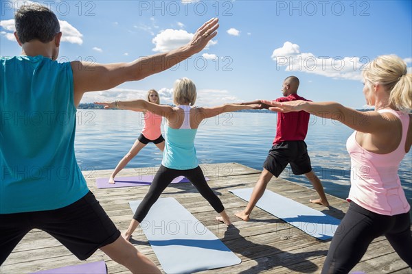Caucasian people practicing yoga on wooden dock