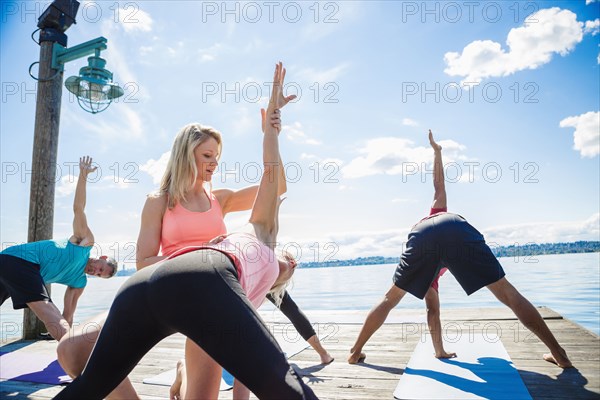 Caucasian people practicing yoga on wooden dock