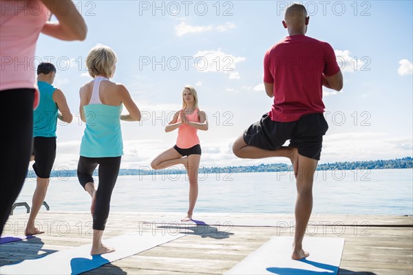 Caucasian people practicing yoga on wooden dock