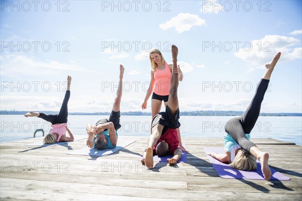 Caucasian people practicing yoga on wooden dock