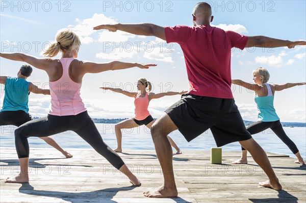 Caucasian people practicing yoga on wooden dock