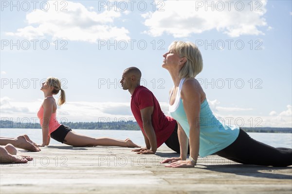 Caucasian people practicing yoga on wooden dock