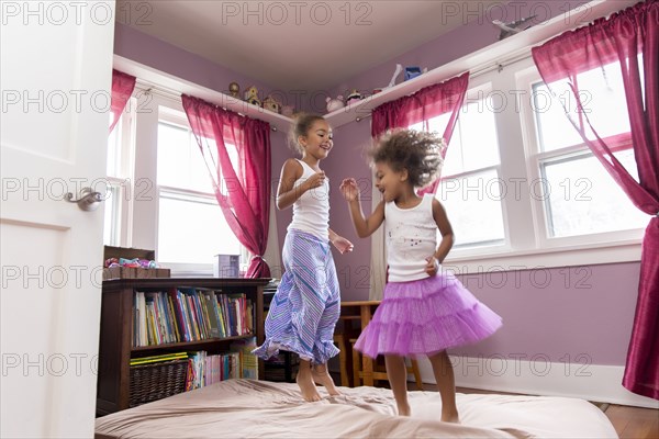 Mixed race girls jumping on bed