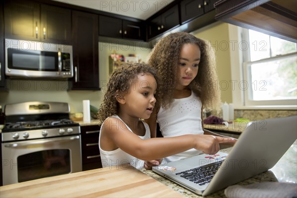 Mixed race girls using laptop in kitchen