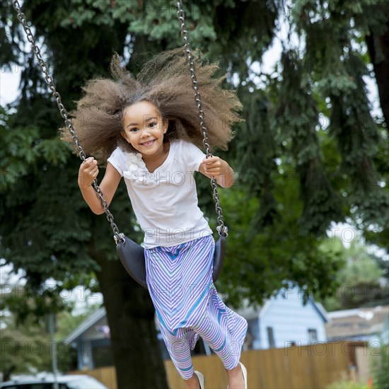 Mixed race girl playing on swing