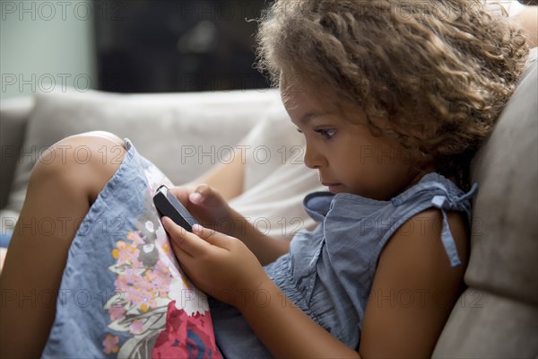 Mixed race girl using cell phone on sofa