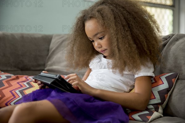 Mixed race girl using digital tablet on sofa