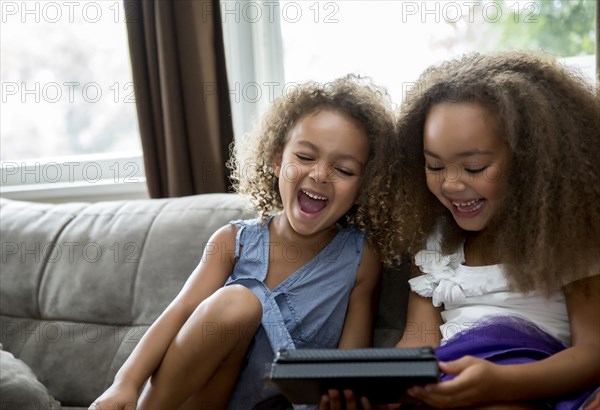 Mixed race girls using digital tablet on sofa