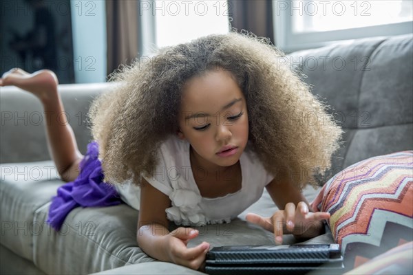 Mixed race girl using digital tablet on sofa