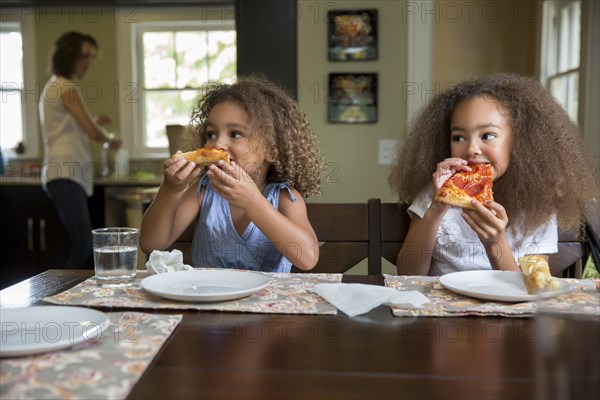 Mixed race girls eating pizza at table