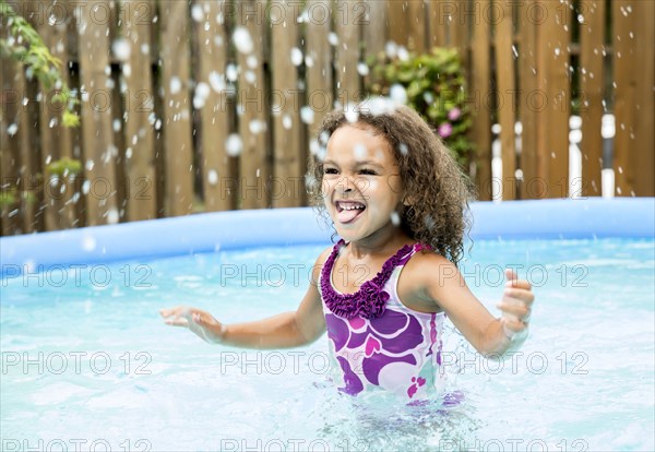 Mixed race girl splashing in swimming pool