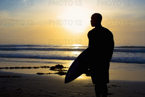 Silhouette of mixed race man holding surfboard on beach