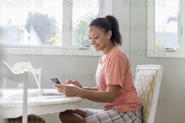 Mixed race woman using laptop and cell phone at table
