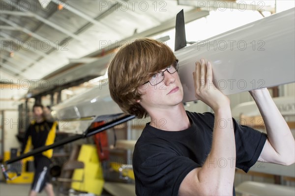 Caucasian boy carrying scull in boathouse