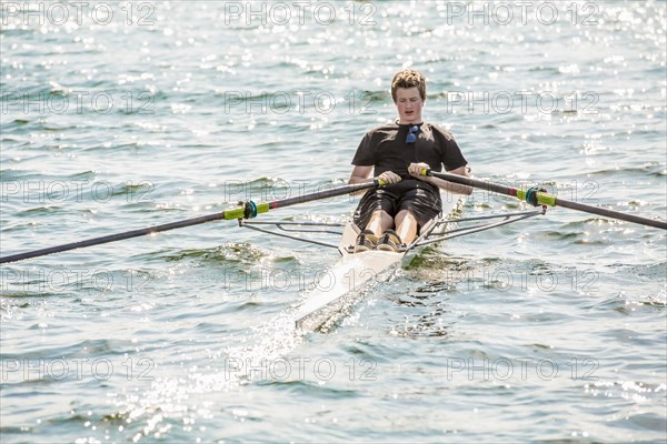 Mixed race teenage boy rowing on lake