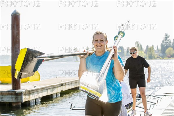 Caucasian teenage girls carrying oars on dock