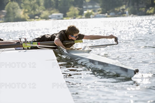 Teenage boy preparing scull from dock over lake