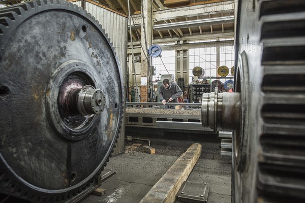 Caucasian man working behind metal cogs in metal shop