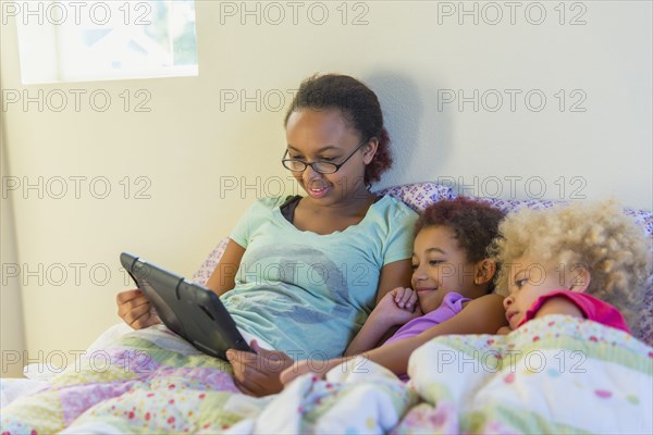 Mixed race sisters using digital tablet in bed