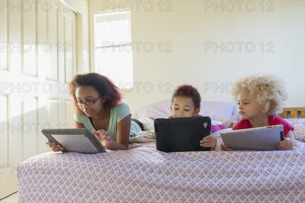 Mixed race sisters using digital tablets in bed